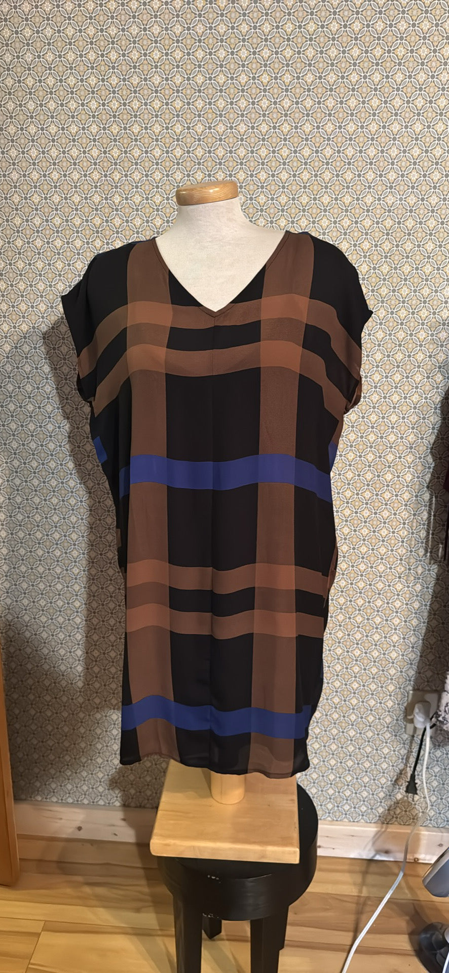 A sleeveless V-neck dress  featuring a plaid pattern with black, brown, and blue stripes