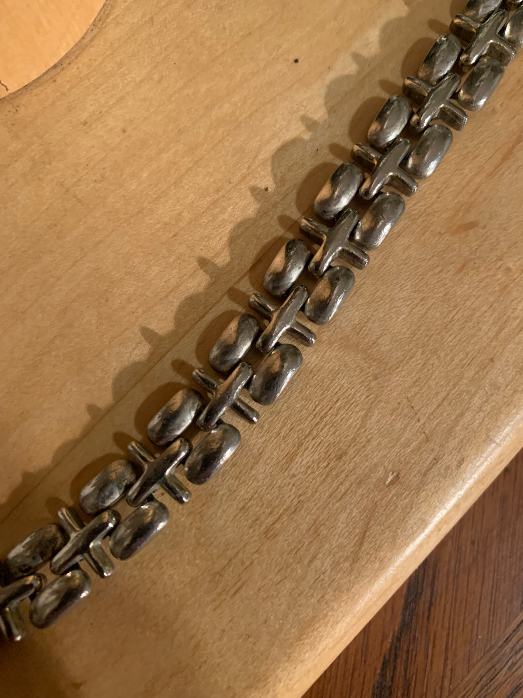 A close-up of a silver-toned metal chain bracelet laid diagonally across a light wood surface.