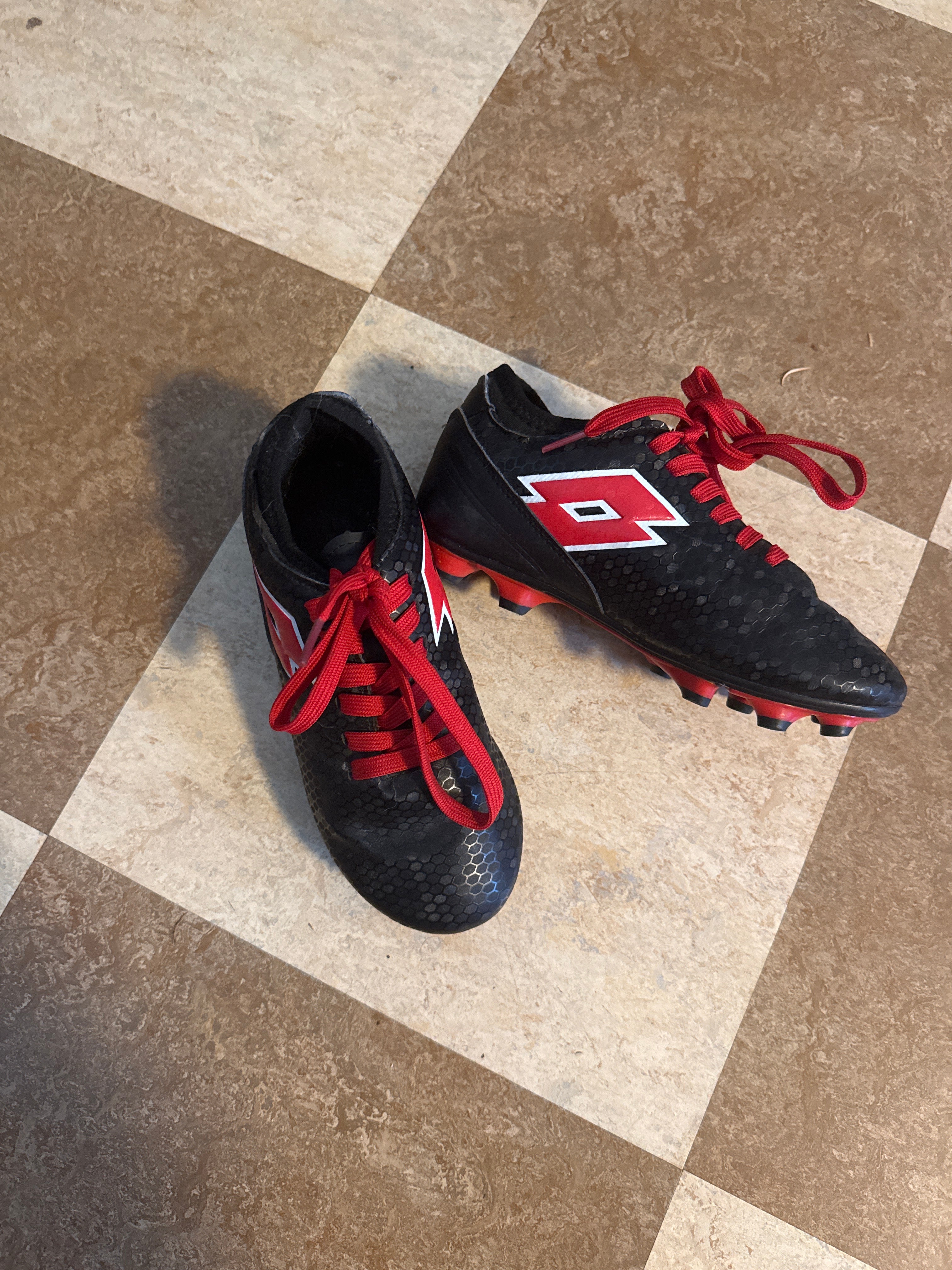 A pair of black soccer cleats with red laces and a red and white logo
