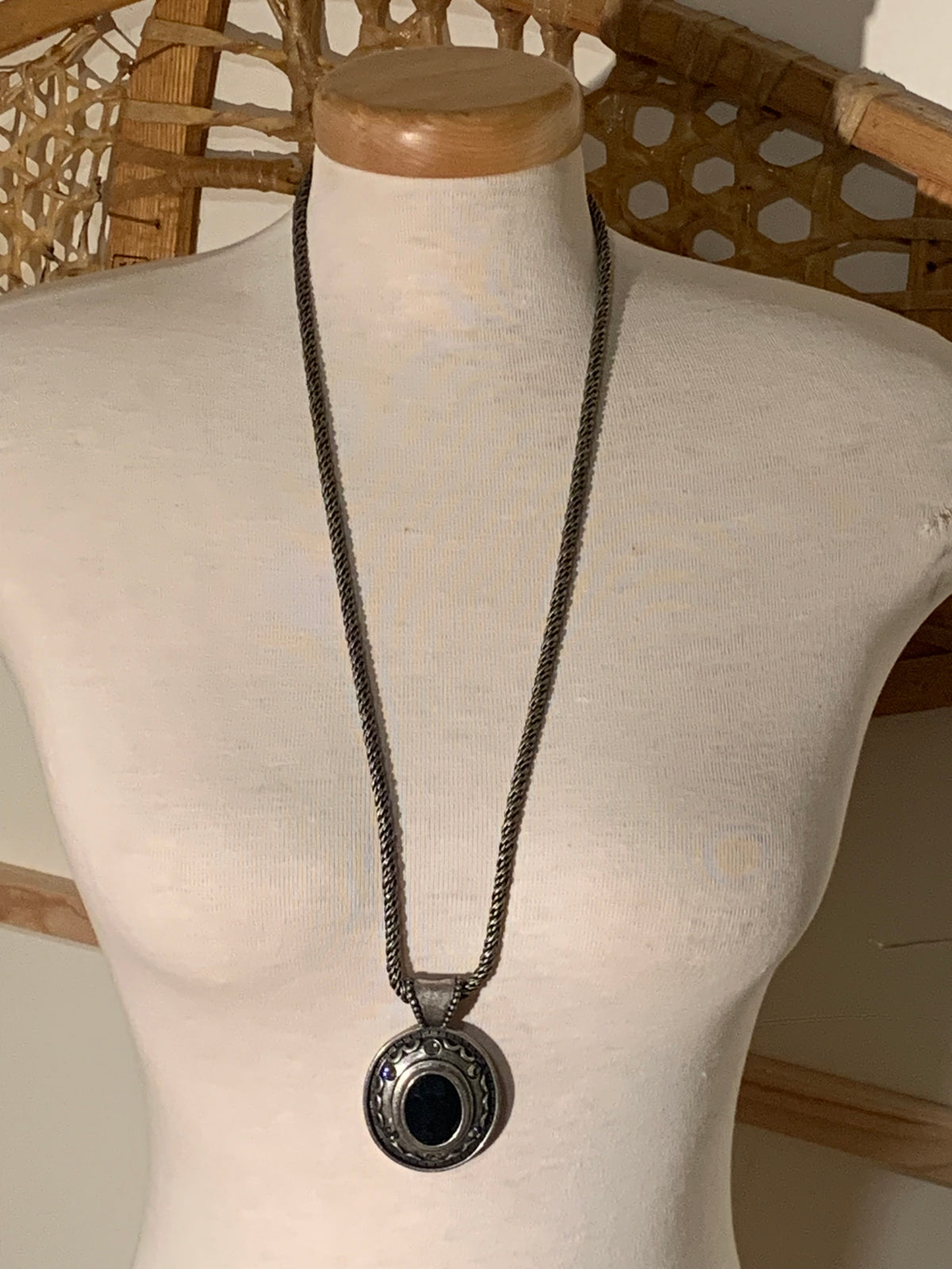 antique silver-toned rope chain, this piece holds a circular pendant with textured, Southwestern-style detailing and a glossy black cabochon centerpiece