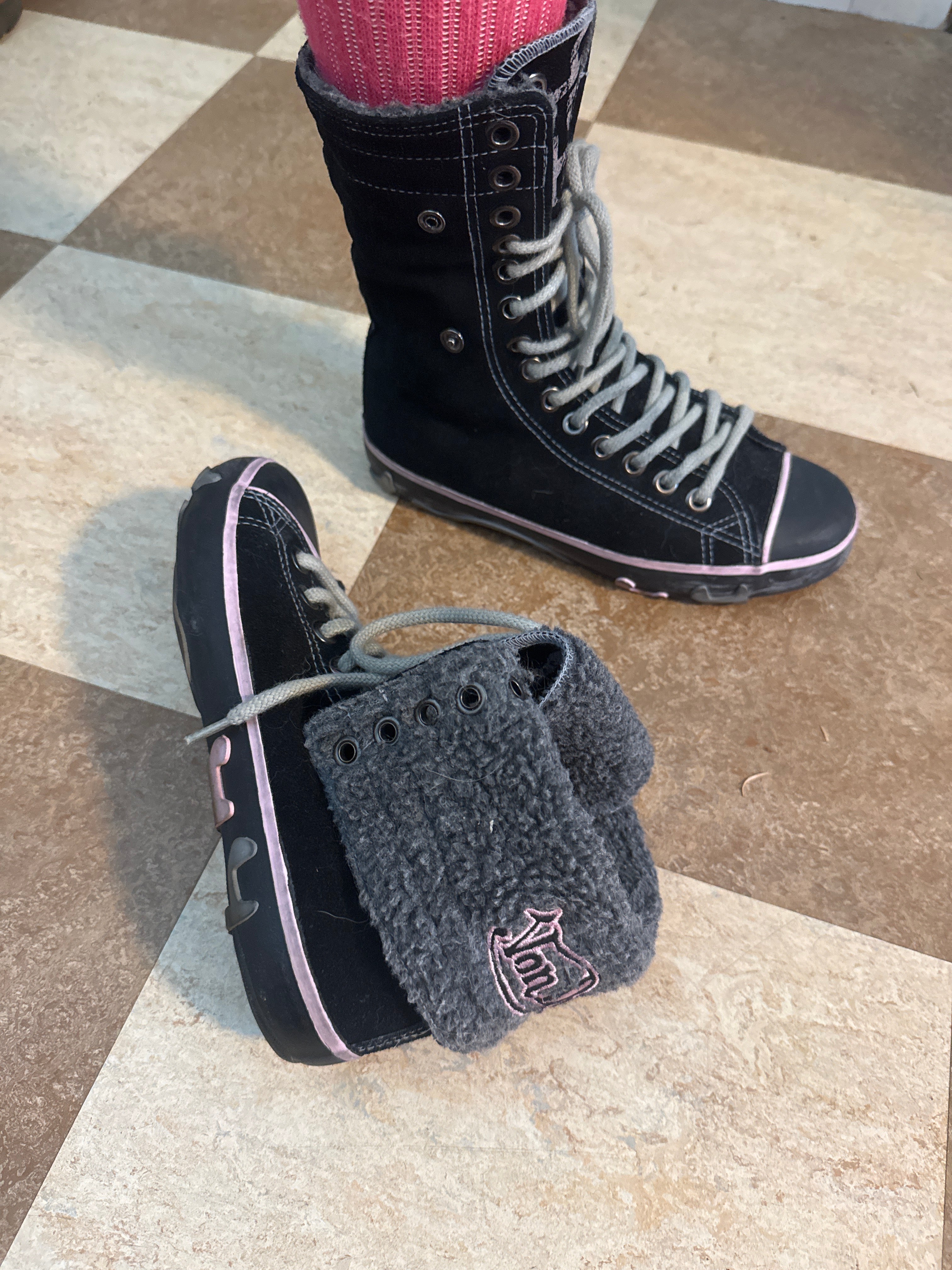 A pair of black high-top Von Dutch sneakers with gray laces and pink trim. A gray fleece collar with a pink embroidered logo is visible on the shoe.