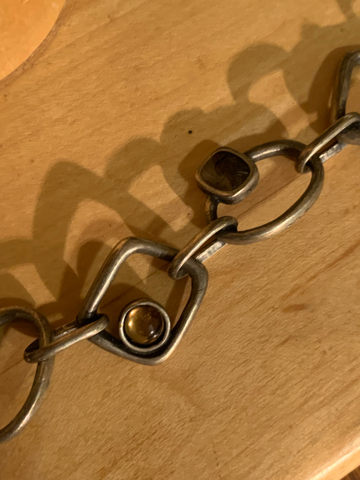 A close-up of a metal link chain bracelet with square and oval links, resting on a light wood surface.