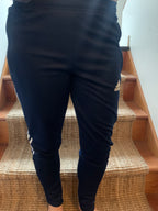 A person wearing black Adidas track pants with white stripes and a small gold logo