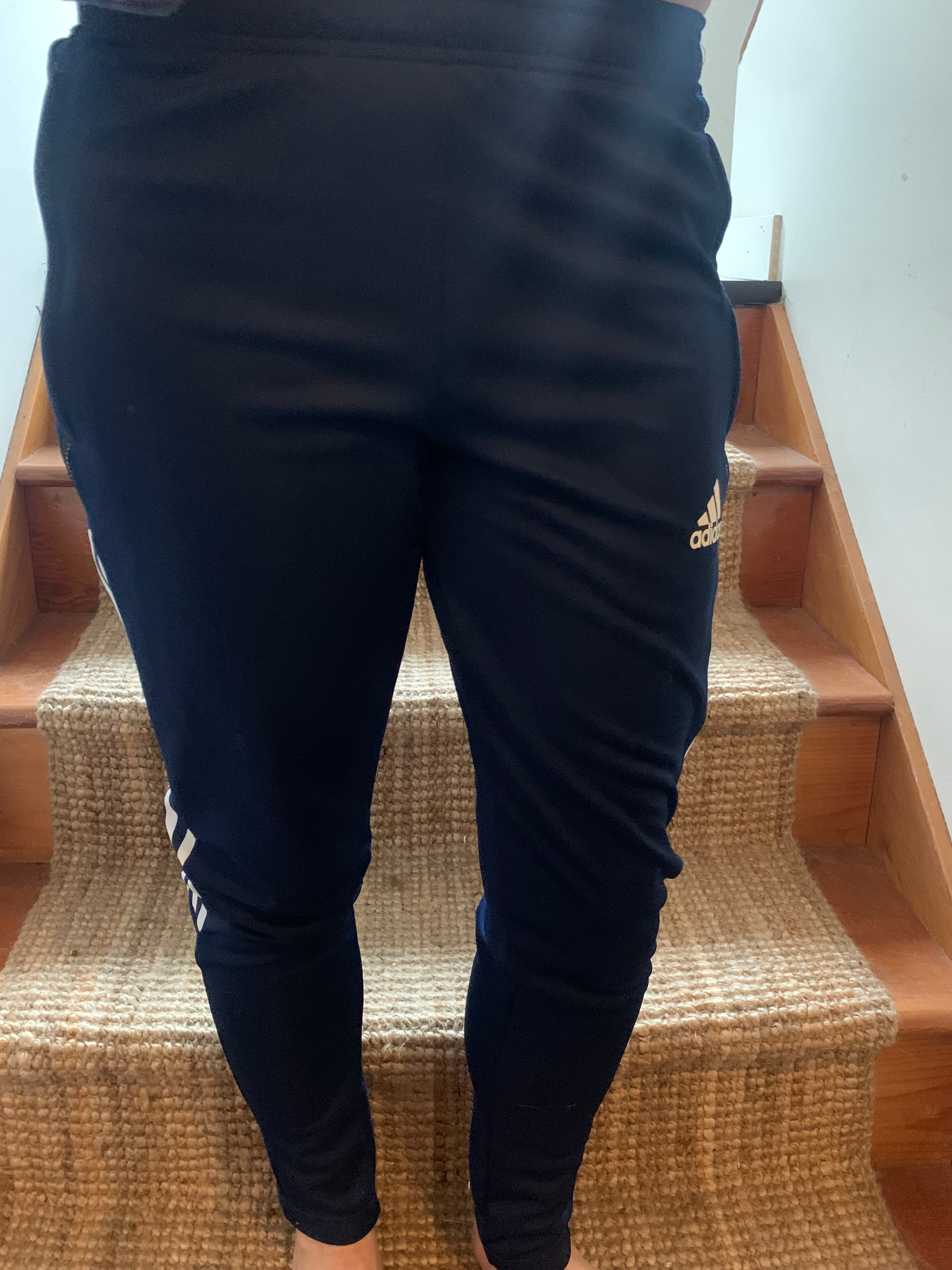 A person wearing black Adidas track pants with white stripes and a small gold logo