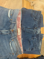 Two pairs of folded blue jeans laid flat on a light wood floor. The top pair is a darker medium-wash blue, and the bottom pair is a lighter washed blue denim 