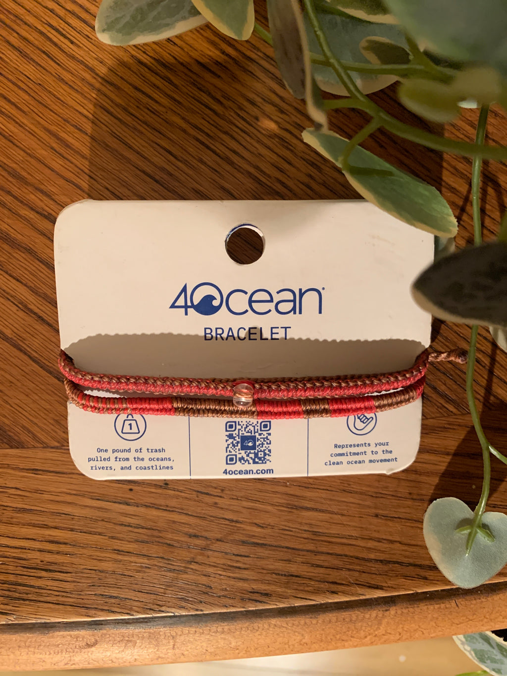 A 40 Ocean bracelet wrapped on its original white cardboard hanger, resting on a wooden surface with green leaves framing the top right corner.
