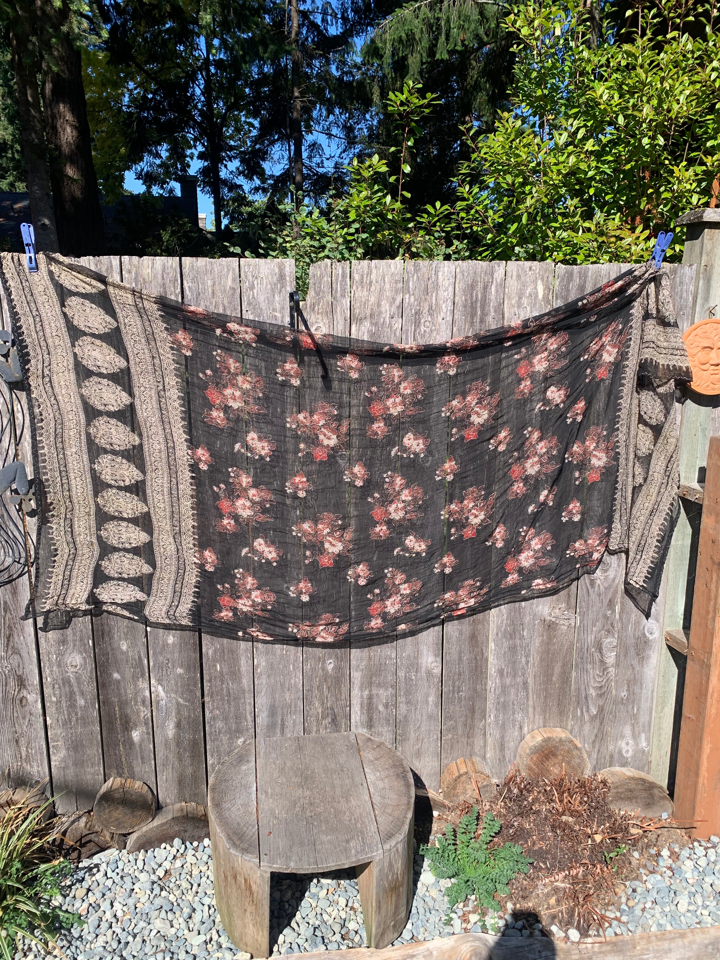 A sheer black scarf with a white and red floral pattern and textured beige borders. The Sheer Black Shawl/Scarf With Red Floral Print is at Vardo Vintage and Valuables online consignment shop and in Parksville BC