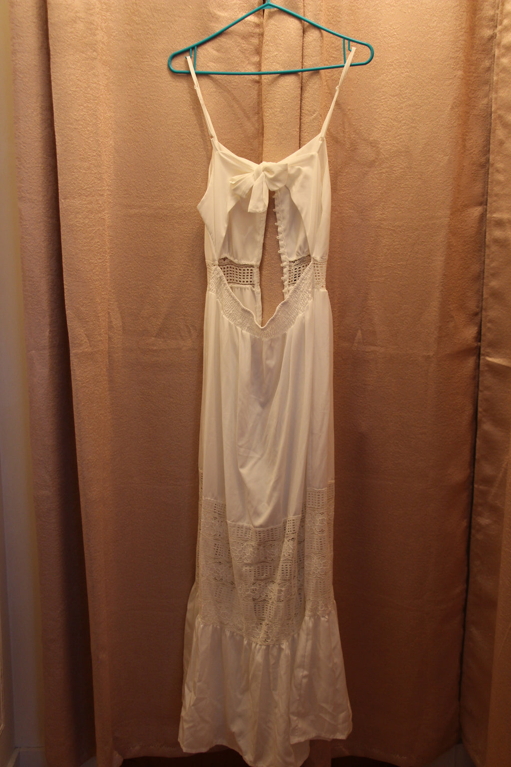 A white sleeveless maxi dress with thin straps, a bow detail at the neckline, and lace panels. A Consignment boutique, Size L White Halter Dress with Button Front Lace Panels and Gathered Hem.