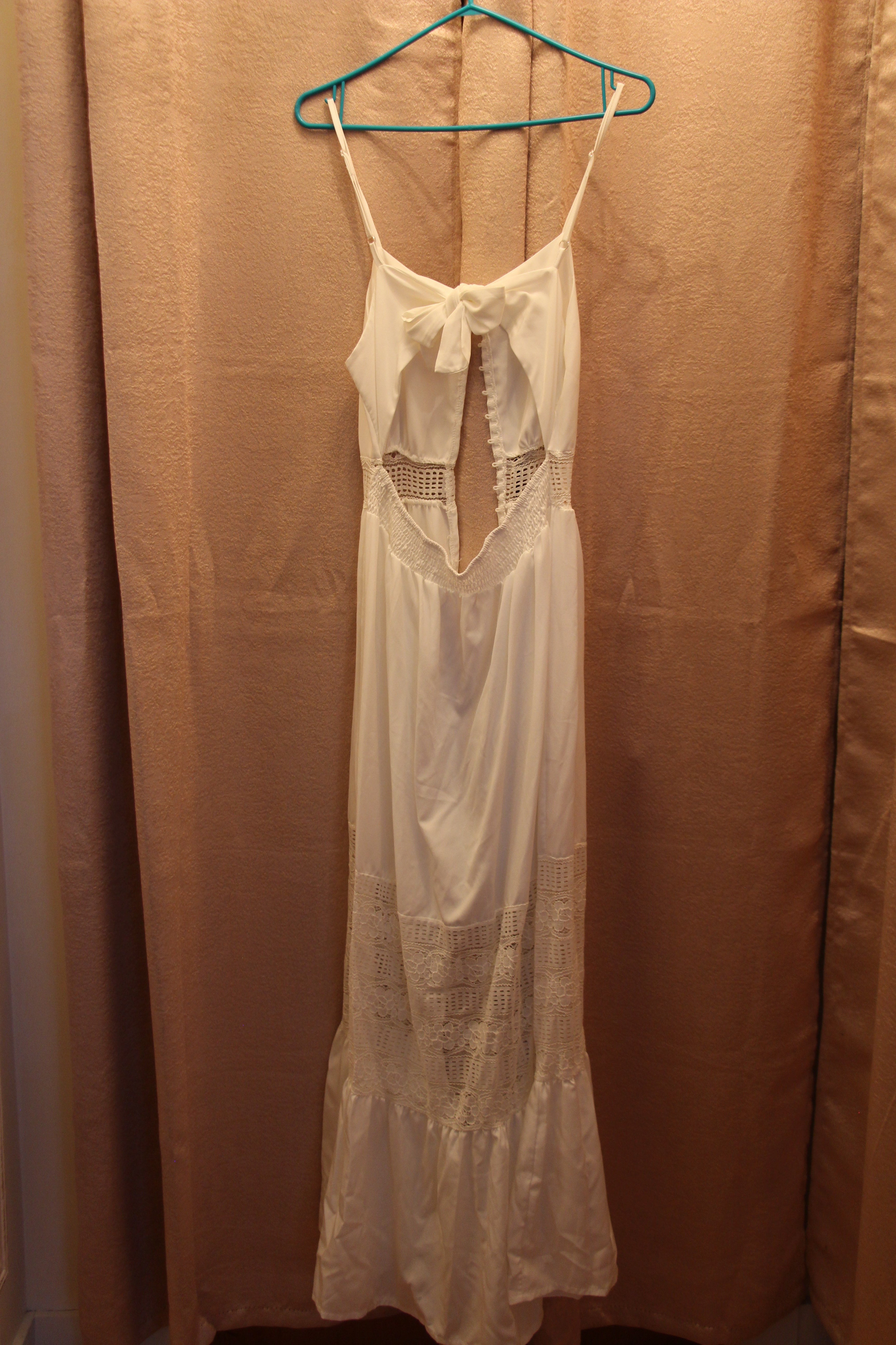 A white sleeveless maxi dress with thin straps, a bow detail at the neckline, and lace panels. A Consignment boutique, Size L White Halter Dress with Button Front Lace Panels and Gathered Hem.