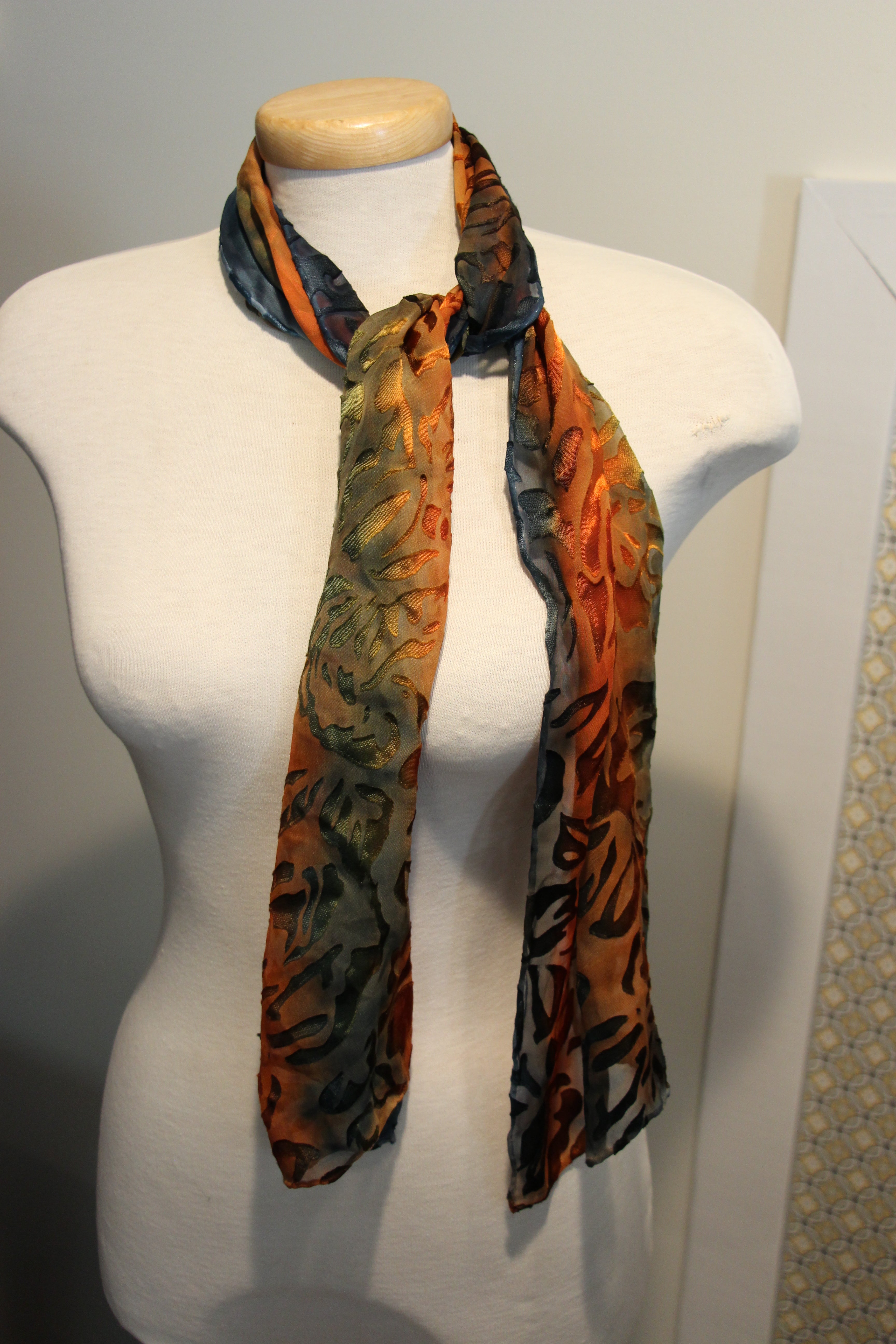 A lightweight scarf with an abstract botanical pattern in orange, olive green, and blue.