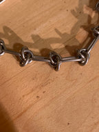 A close-up of a chunky silver metal chain link bracelet resting on a light brown wooden surface.