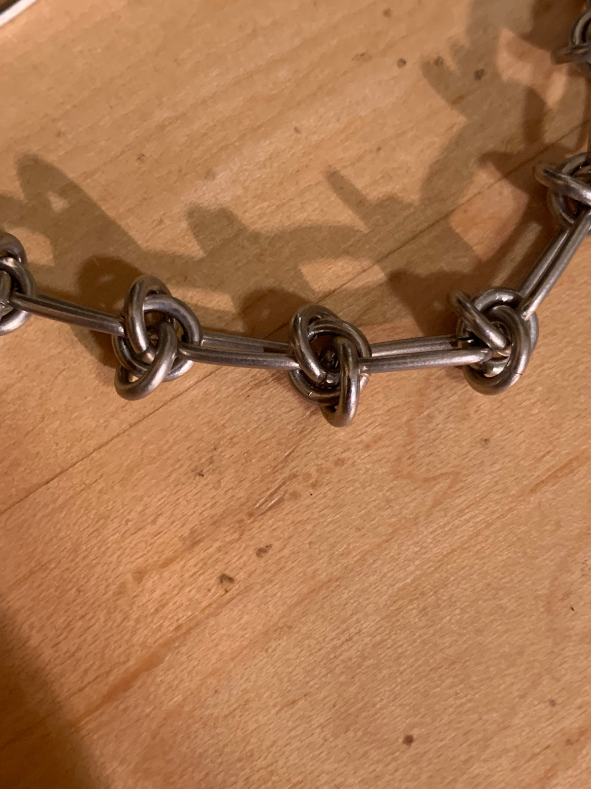 A close-up of a chunky silver metal chain link bracelet resting on a light brown wooden surface.