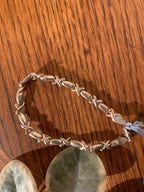 A handmade silver-toned beaded bracelet with twisted links, displayed on a wooden surface with decorative green leaves.