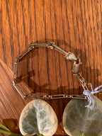 A silver-toned chain bracelet with a lobster clasp, displayed on a wooden surface with two green-and-white patterned stones.