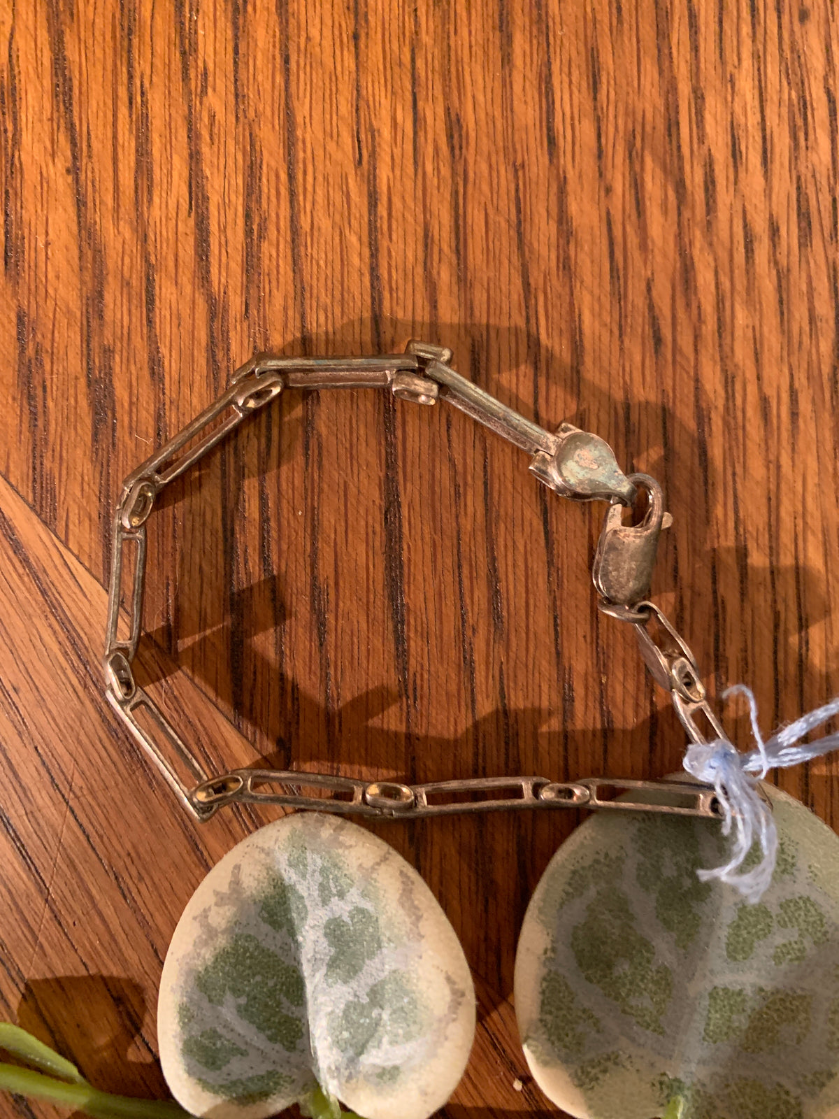 A silver-toned chain bracelet with a lobster clasp, displayed on a wooden surface with two green-and-white patterned stones.